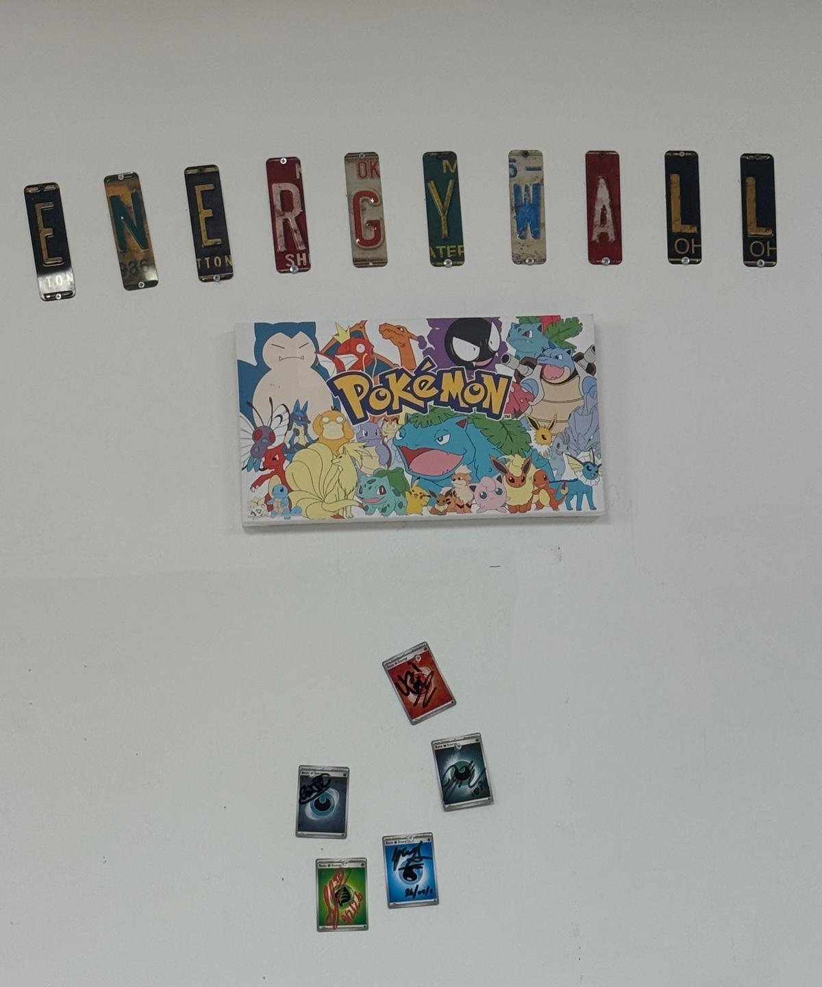 The Energy Wall — a sign made from license plate letters spelling ENERGY WALL, a Pokémon plaque, and fan-signed Energy cards pinned to the wall